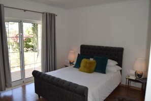 Ein Schlafzimmer mit einem großen Bett, zwei Nachttischen und Blick durch eine Glasschiebetür.