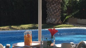 Ein Tisch mit einem Buch, einem Glas Orangensaft, einer weißen Tasse und einer Vase mit einer roten Blume am Pool.