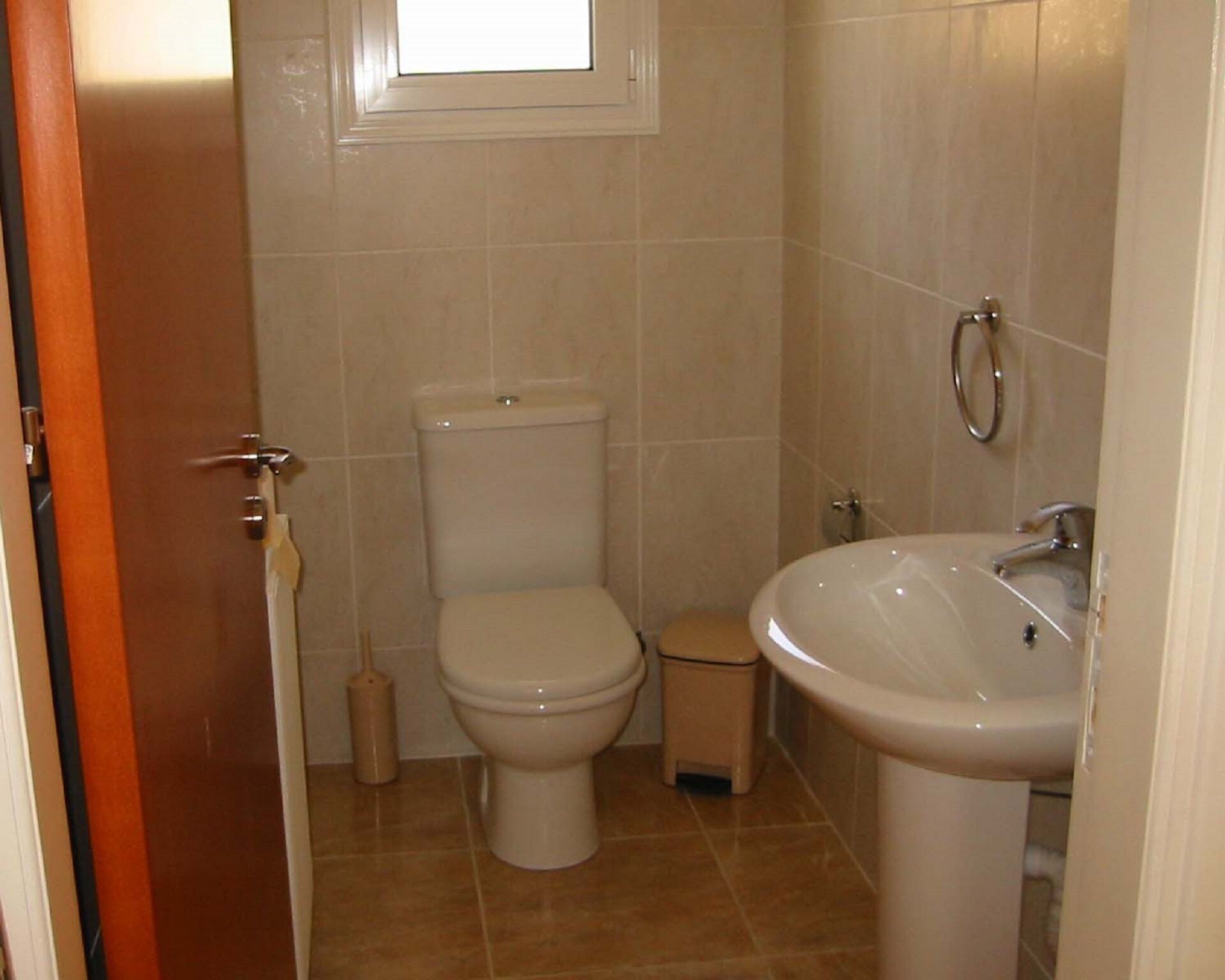 A small bathroom with a toilet, a sink, and a window above the toilet.
