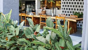 An outdoor seating area with wooden tables and chairs, surrounded by large green plants. - ISTY Hotel (Chiang Mai)