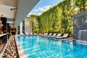 A swimming pool with lounge chairs, a bar area, and a wall with a climbing plant. - ISTY Hotel (Chiang Mai)