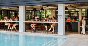 An outdoor pool area with people dining at tables, a bar area, and a sign indicating a swimming pool. - ISTY Hotel (Chiang Mai)