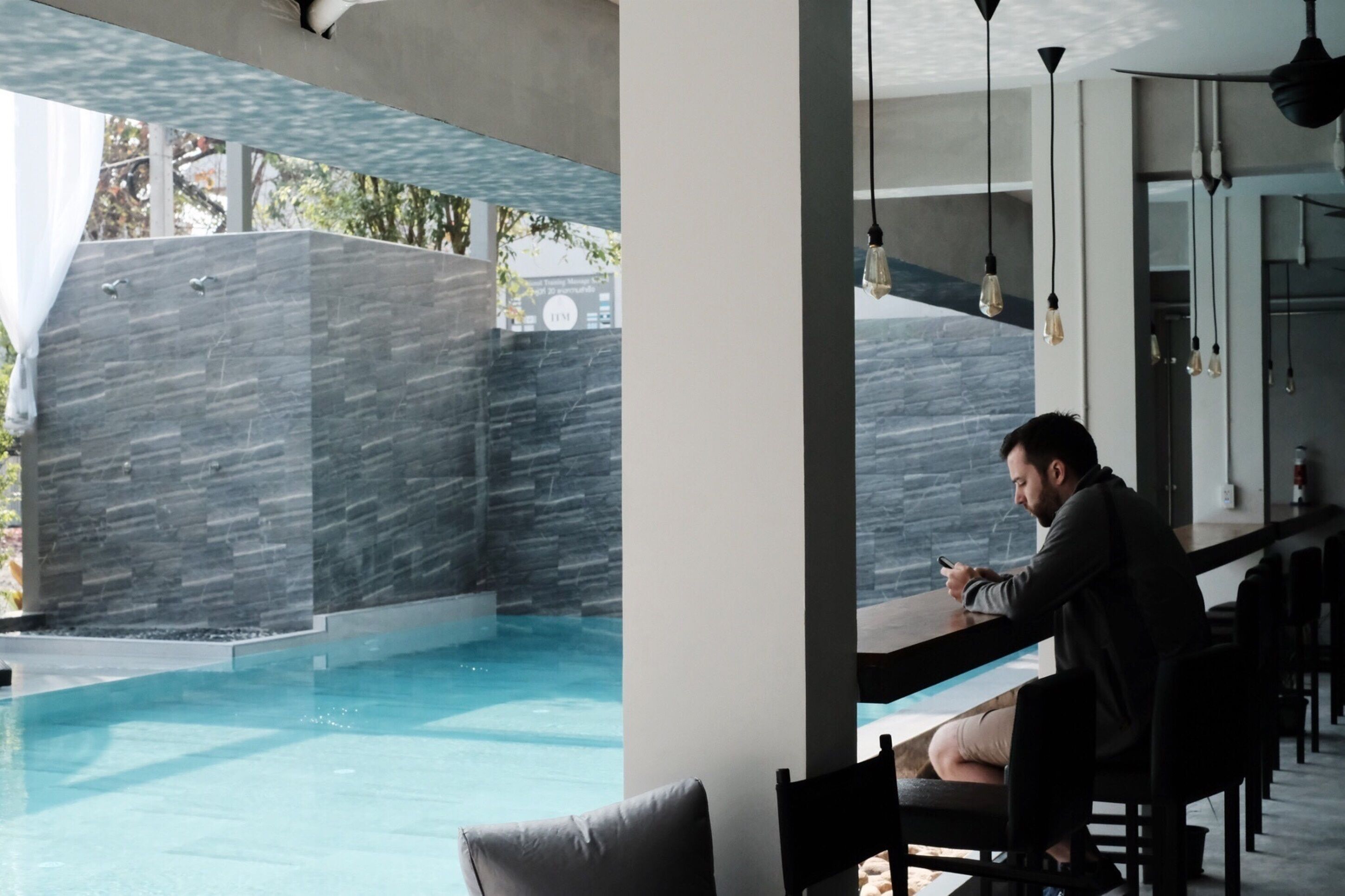 A modern indoor pool area with a stone wall and a person sitting at a bar.