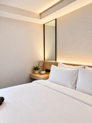 A hotel room with a large bed, a bedside table with a lamp, and a mirror. - ISTY Hotel (Chiang Mai)
