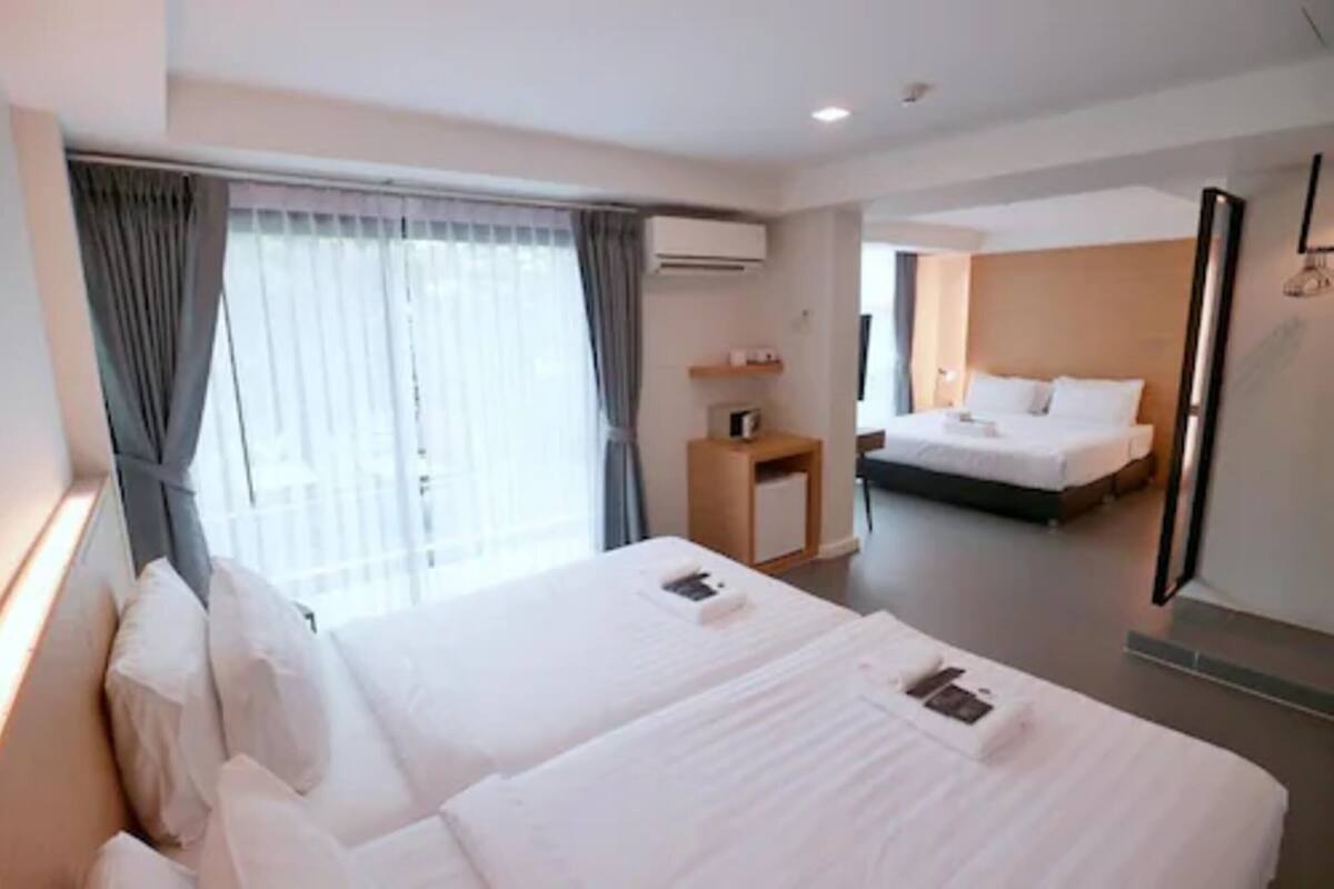 A hotel room with two beds, a small bedside table, a mirror, and a window with curtains.