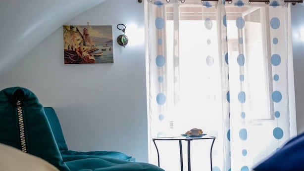 Ein Zimmer mit einem türkisfarbenen Sofa, einem kleinen Tisch mit Tasse und Teller, und einem Bild an der Wand.