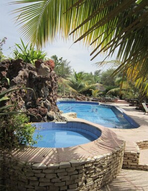 Une piscine avec un mur en pierre et des palmiers en arrière-plan.
