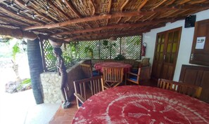 Un espace extérieur abrité, avec une table et des chaises, un toit de chaume et un mur en pierre.