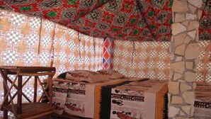 A room with a bed covered in patterned bedding, a wooden chair, and a stone wall.