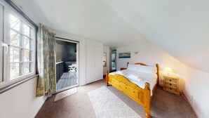 Une chambre à coucher avec un lit en bois, une petite table de chevet, une commode et une fenêtre avec des rideaux.
