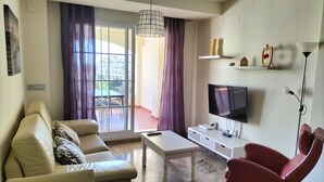 Un saló amb un sofà, una butaca, televisió i un balcó amb taula i cadires.