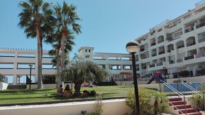 Un pati d'hotel amb palmeres, un parc infantil i una escala que mena al edifici.