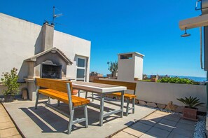 Eine Terrasse im Freien mit einem Grill, Holzbanken und Blick auf das Meer.