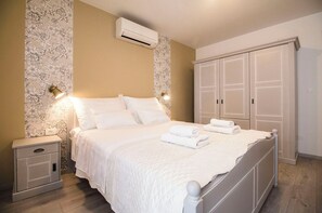A neatly made bed with white linens and a quilted blanket, a bedside table with a lamp, and a wardrobe with double doors.