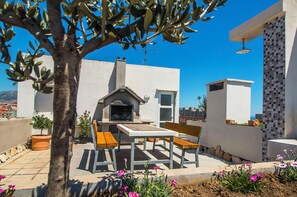 Eine Terrasse im Freien mit Grill, Holzbänken und Topfpflanzen.