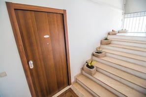 Een houten deur met een naambord, beige treden en plantenbakken.