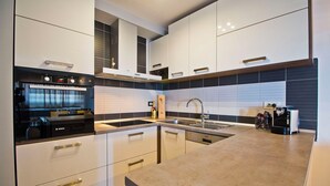 A modern kitchen with white cabinets, a built-in oven, a sink, and a coffee machine.