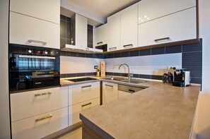 A modern kitchen with white cabinets, a built-in oven, a sink, and a coffee machine.