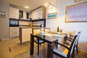 Een moderne keuken met witte kasten, een inbouwoven en een eethoek met een glazen tafel en stoelen.