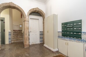 Un pasillo con una puerta blanca, una escalera y un armario verde con varios cajones.