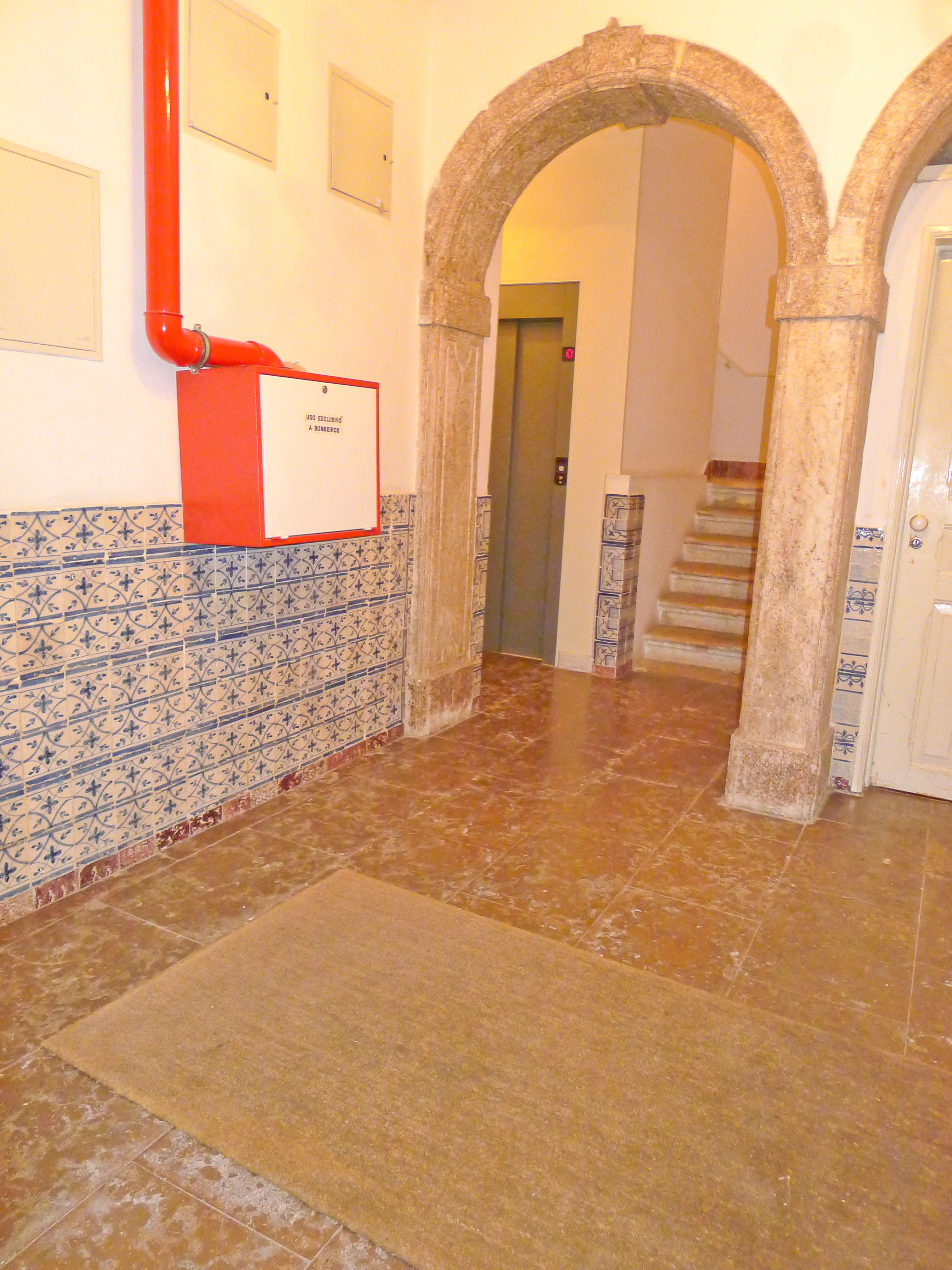 A hallway with tiled walls, a red fire hose, a sign, and a staircase.