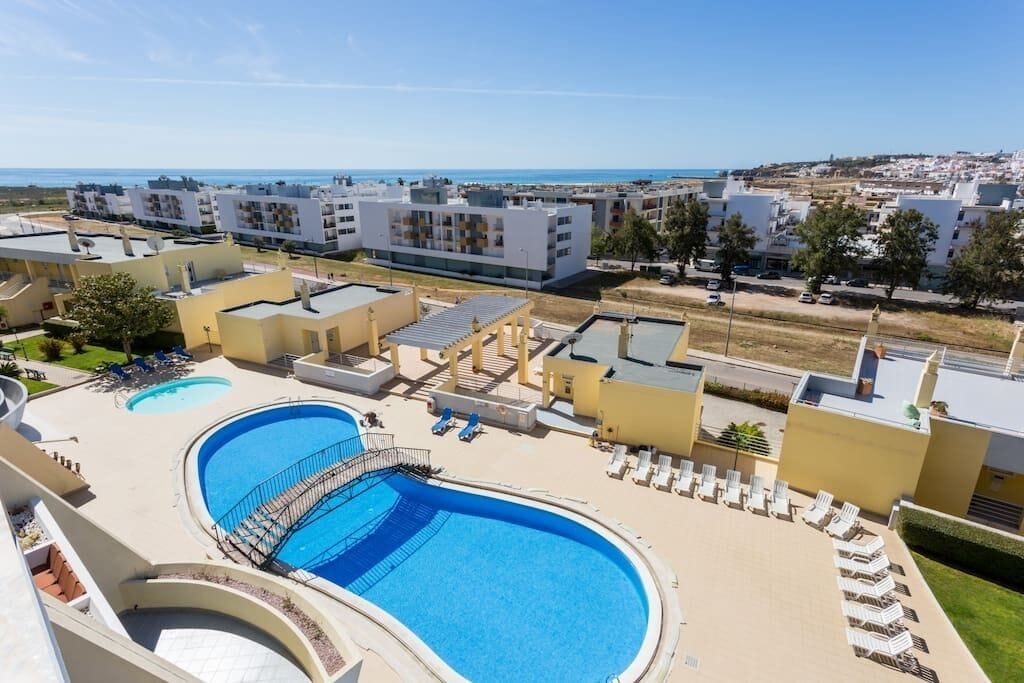 A resort with a large pool, sun loungers, and a view of the sea.