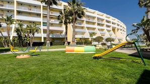 Un hôtel doté d’un grand bâtiment à plusieurs étages, d’une cour verdoyante avec des jeux pour enfants et de palmiers.