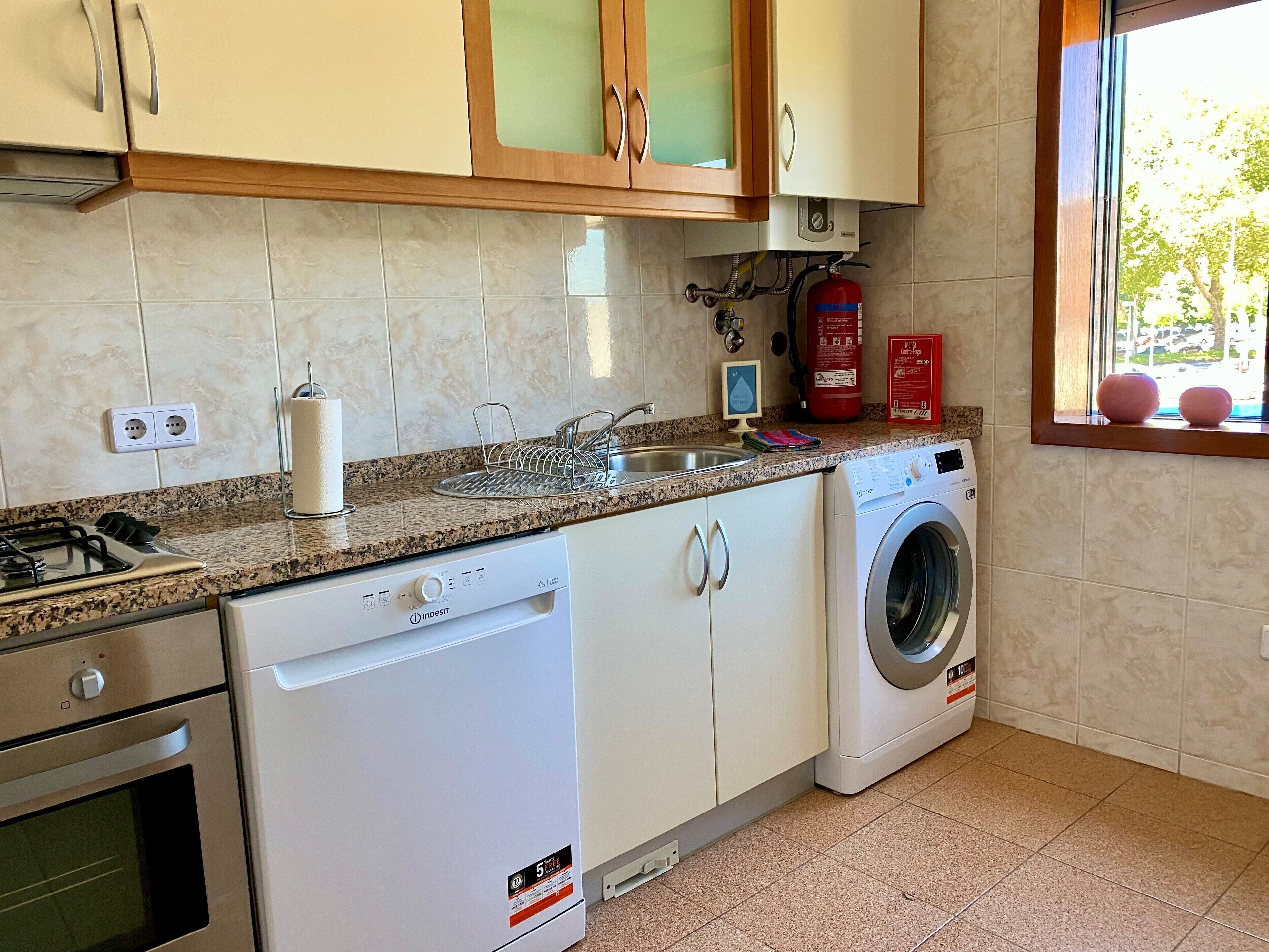 A kitchen with a dishwasher, washing machine, stove, and a window with a view.