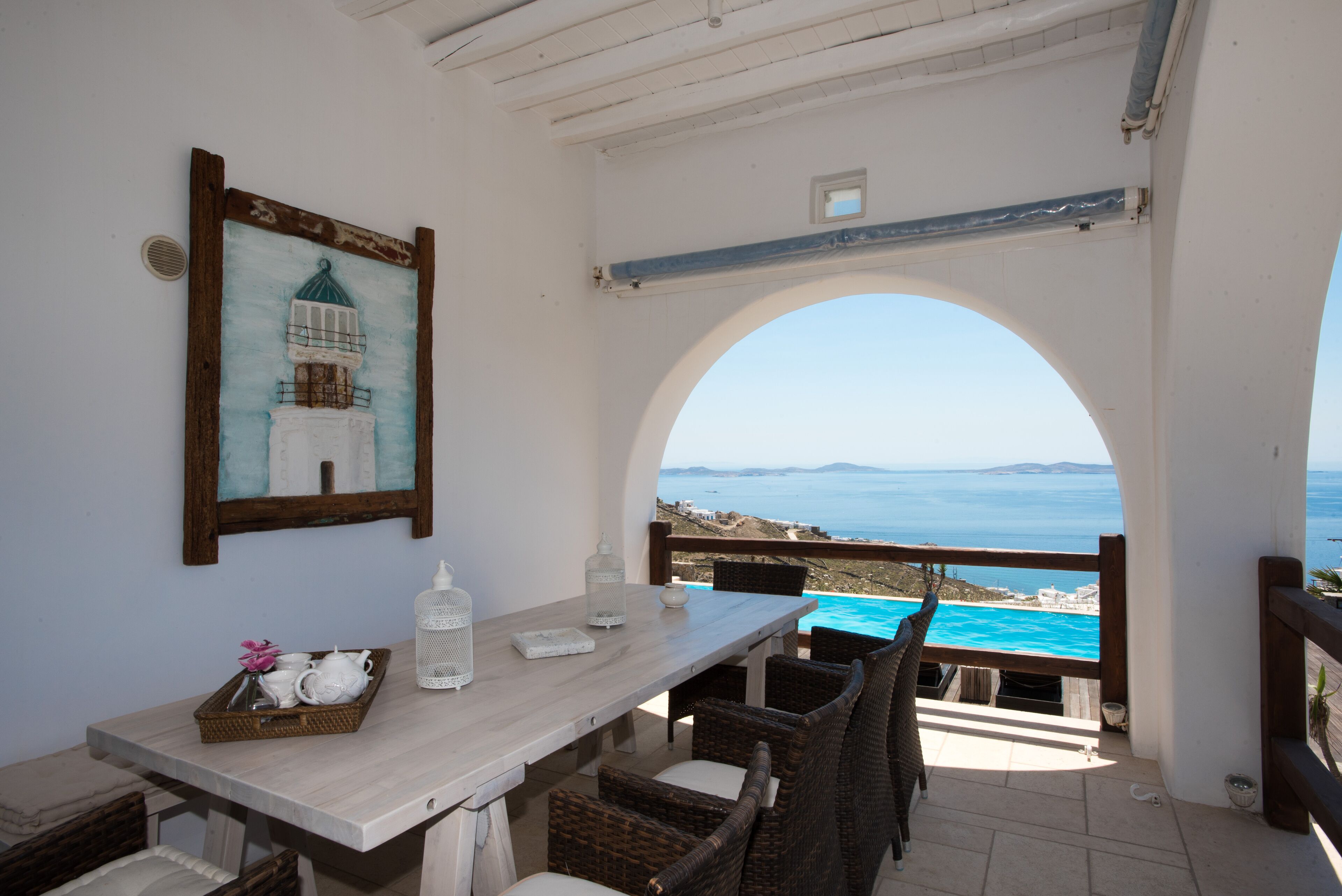Un comedor con vista al mar, un cuadro enmarcado de un faro y mobiliario de mimbre.