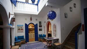 En traditionell marockansk interiör med en innergård, blå dörrar, mönstrade mattor och en trappa.