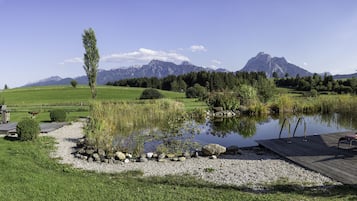 A lakeside deck with outdoor furniture, a barbecue area, and a view of mountains in the background.