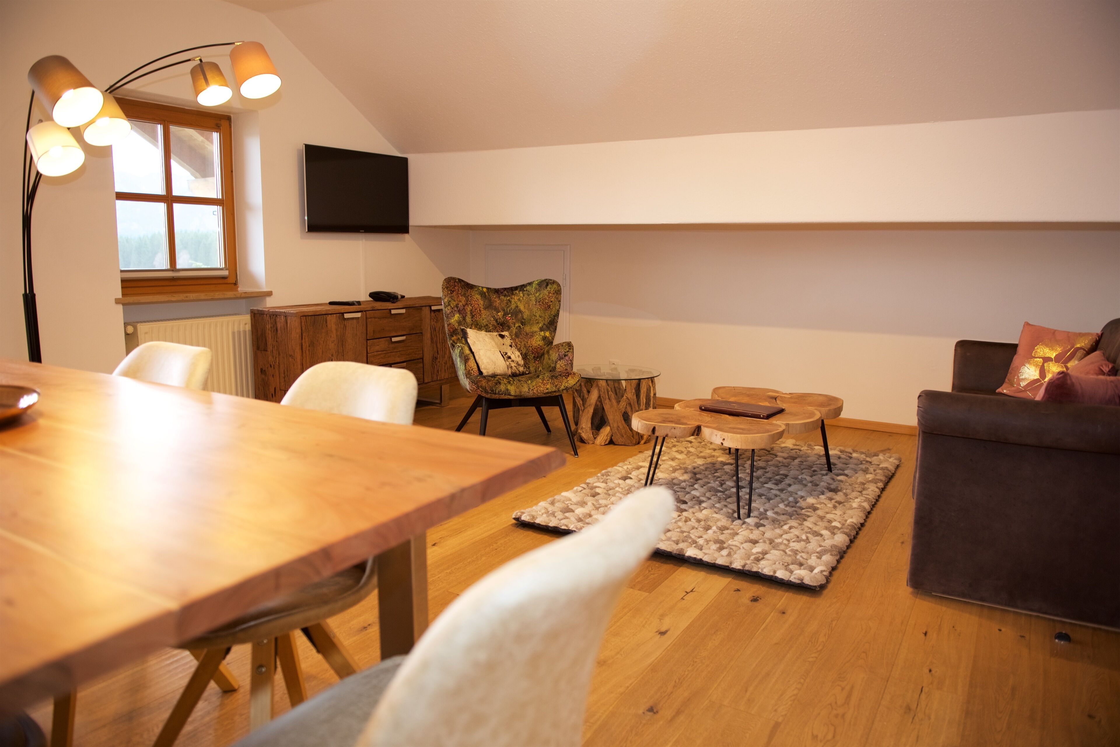 Un salon chaleureux avec une table à manger en bois, un canapé confortable et un téléviseur fixé au mur.