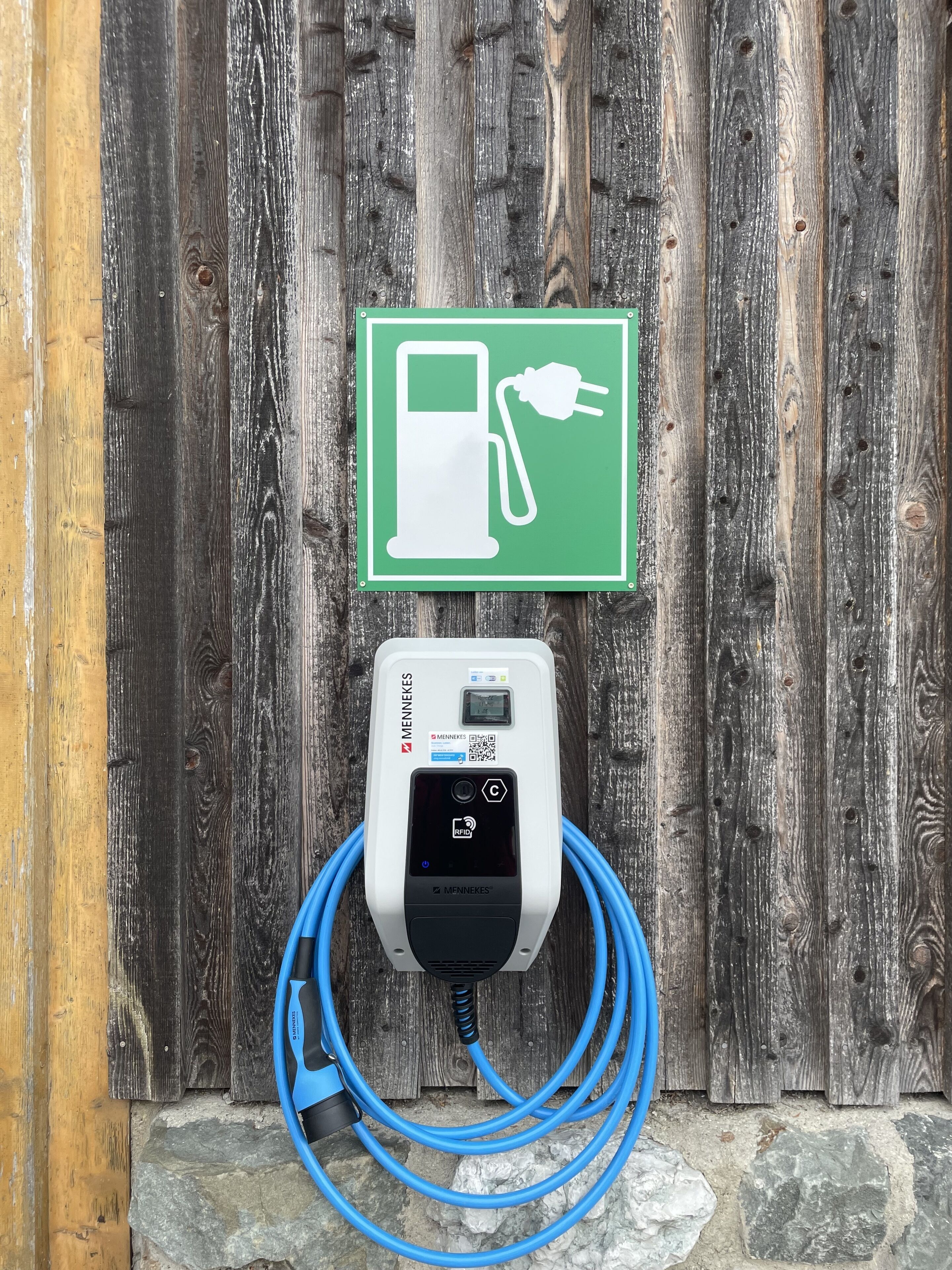 Une borne de recharge avec un panneau vert, un appareil de recharge blanc et un câble bleu, le tout sur un fond en bois.