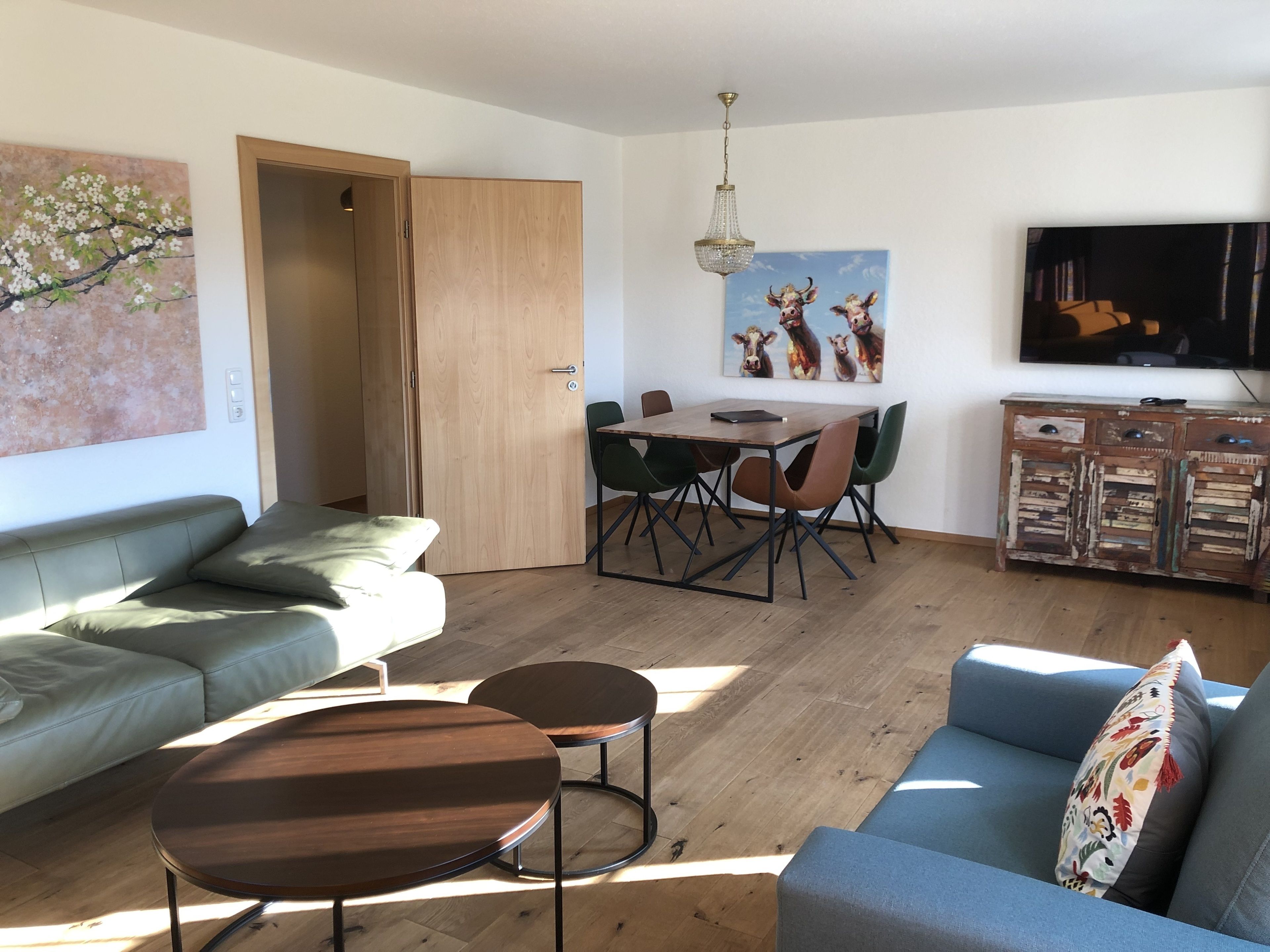 A living room with a sofa, two coffee tables, a dining table with chairs, a TV, and artwork on the walls.