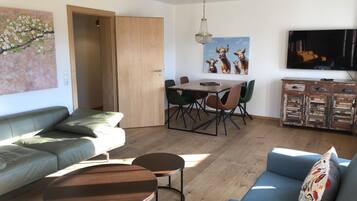 A living room with a sofa, two coffee tables, a dining table with chairs, a TV, and artwork on the walls.