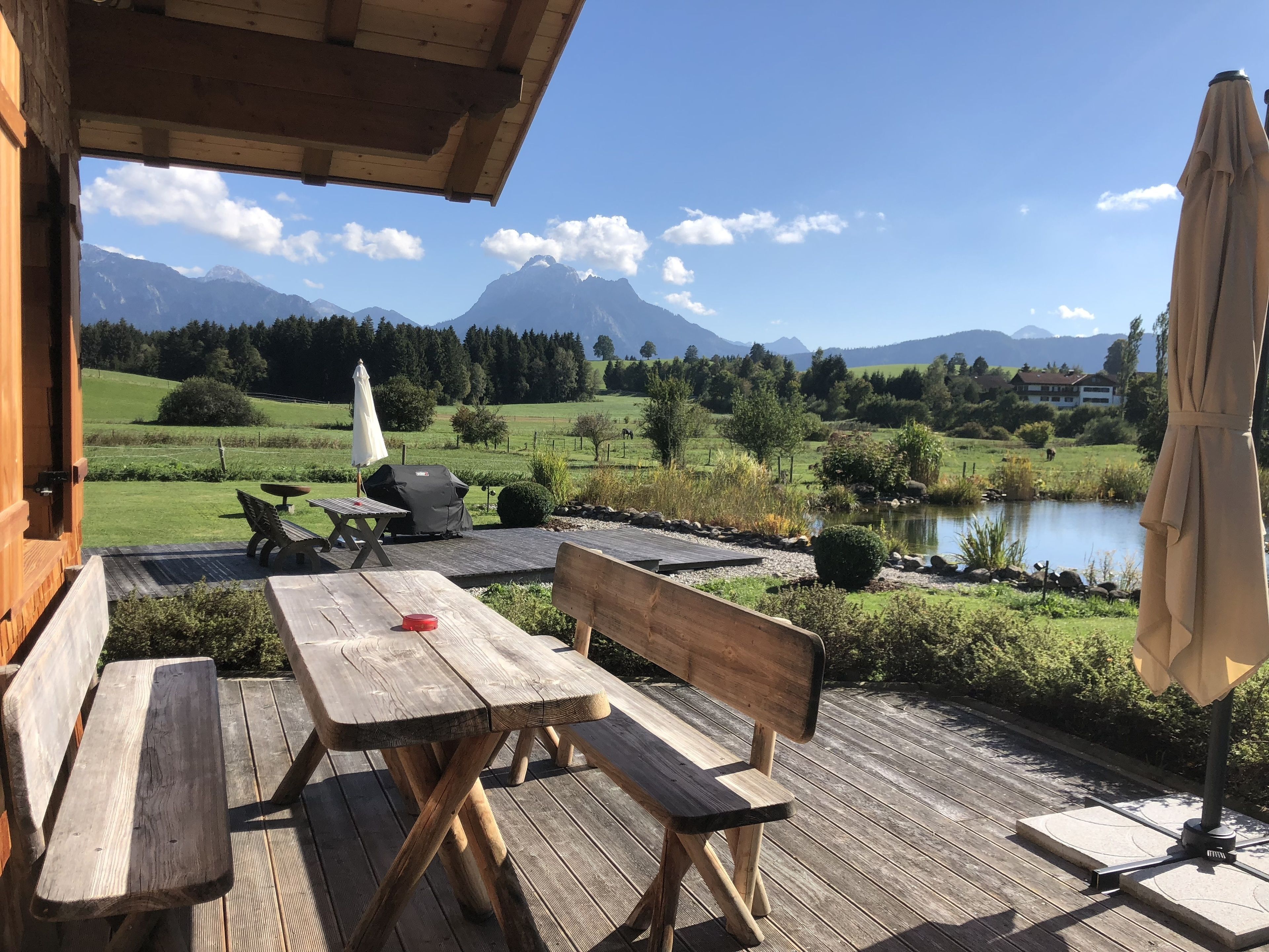 A wooden deck with picnic tables and benches, overlooking a lake and mountains.
