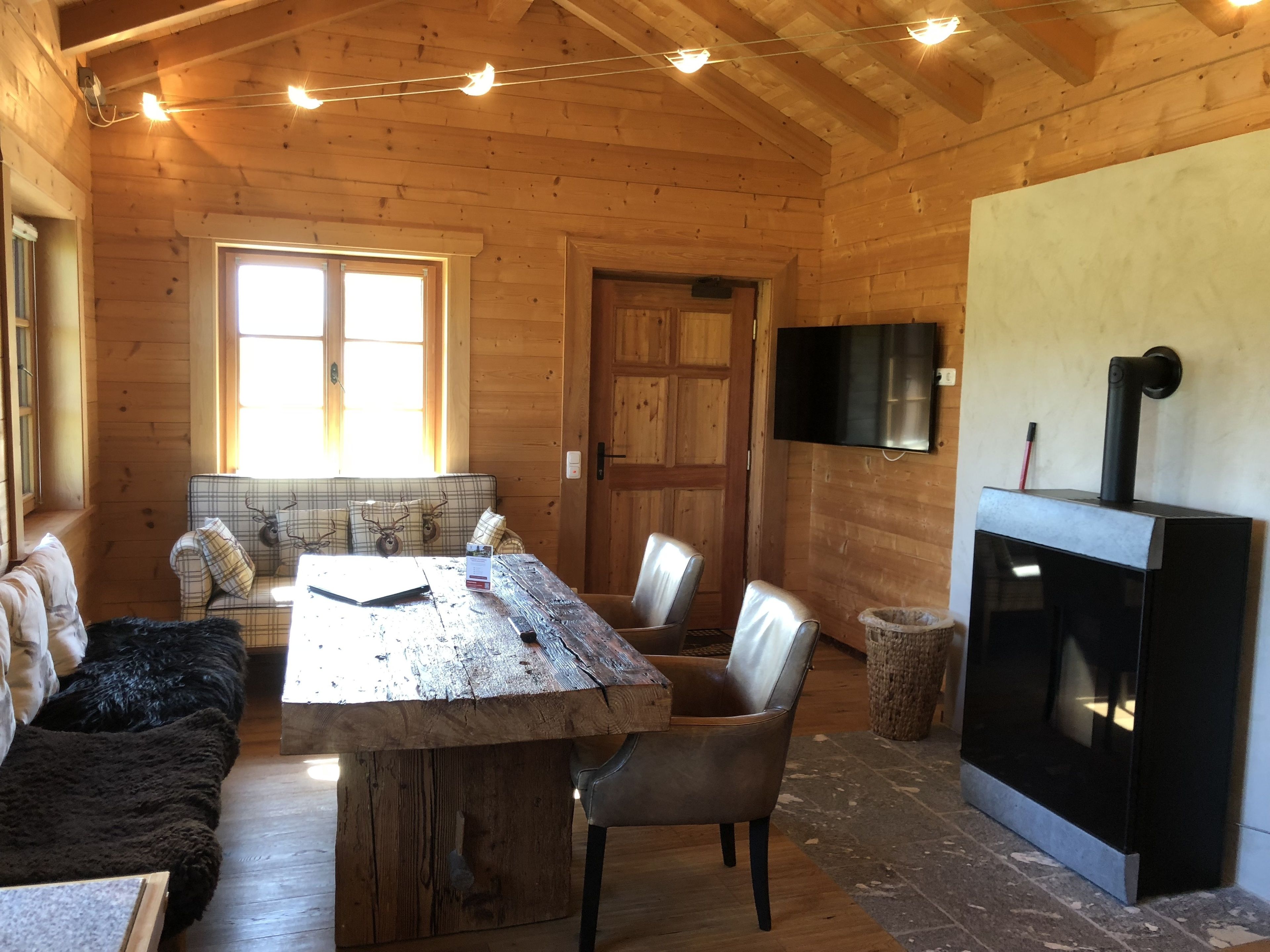 Un interior de cabaña acogedor, con una mesa de comedor de madera, sillas, un sofá, chimenea y televisor montado en la pared.