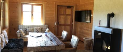 Un interior de cabaña acogedor, con una mesa de comedor de madera, sillas, un sofá, chimenea y televisor montado en la pared.