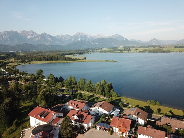 A lakeside residential area with houses, a small marina, and mountains in the background. - Landhaus Kössel (Fuessen)
