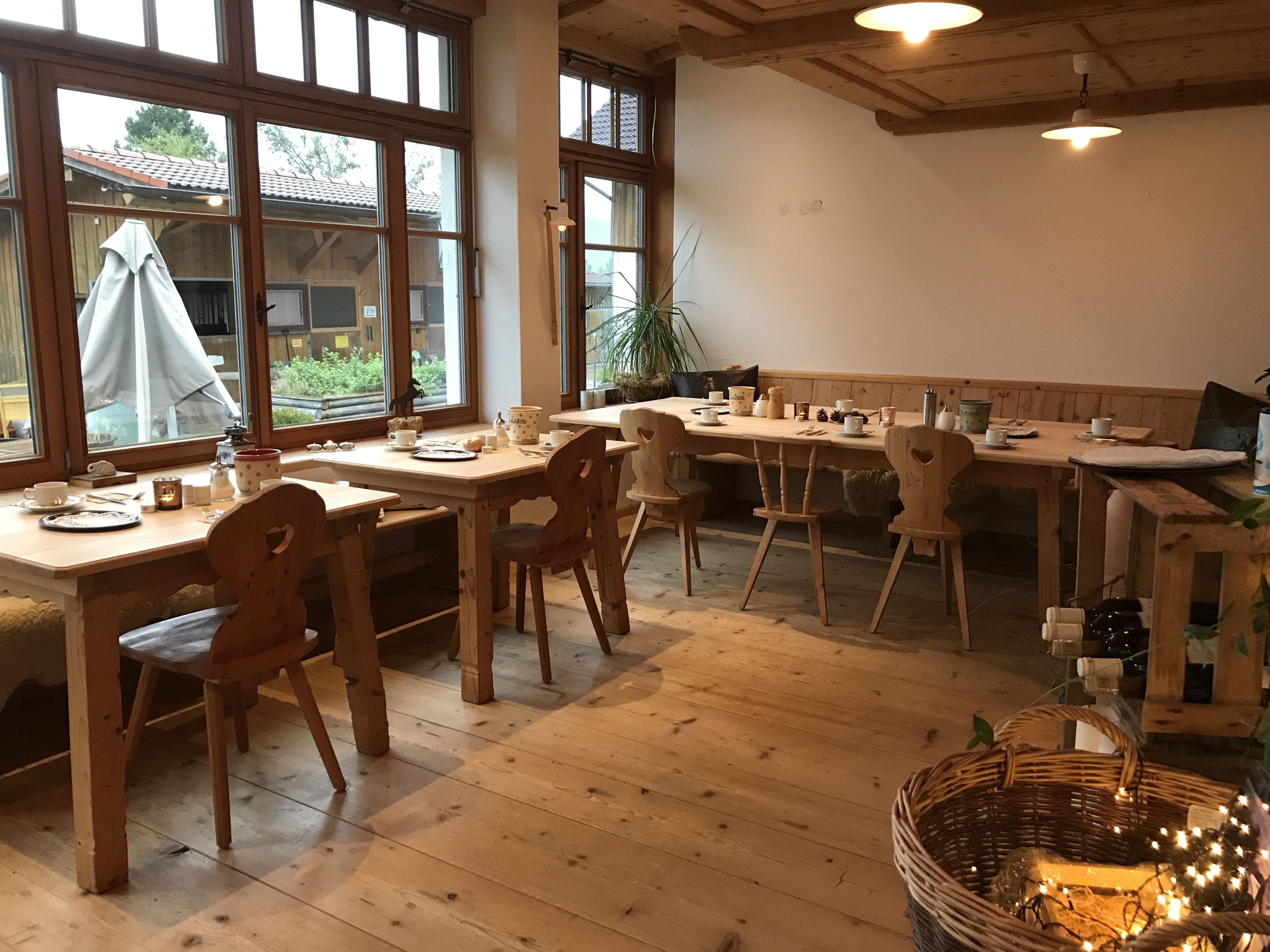 A cozy dining area with wooden tables and chairs, large windows, and a view of the outdoors.