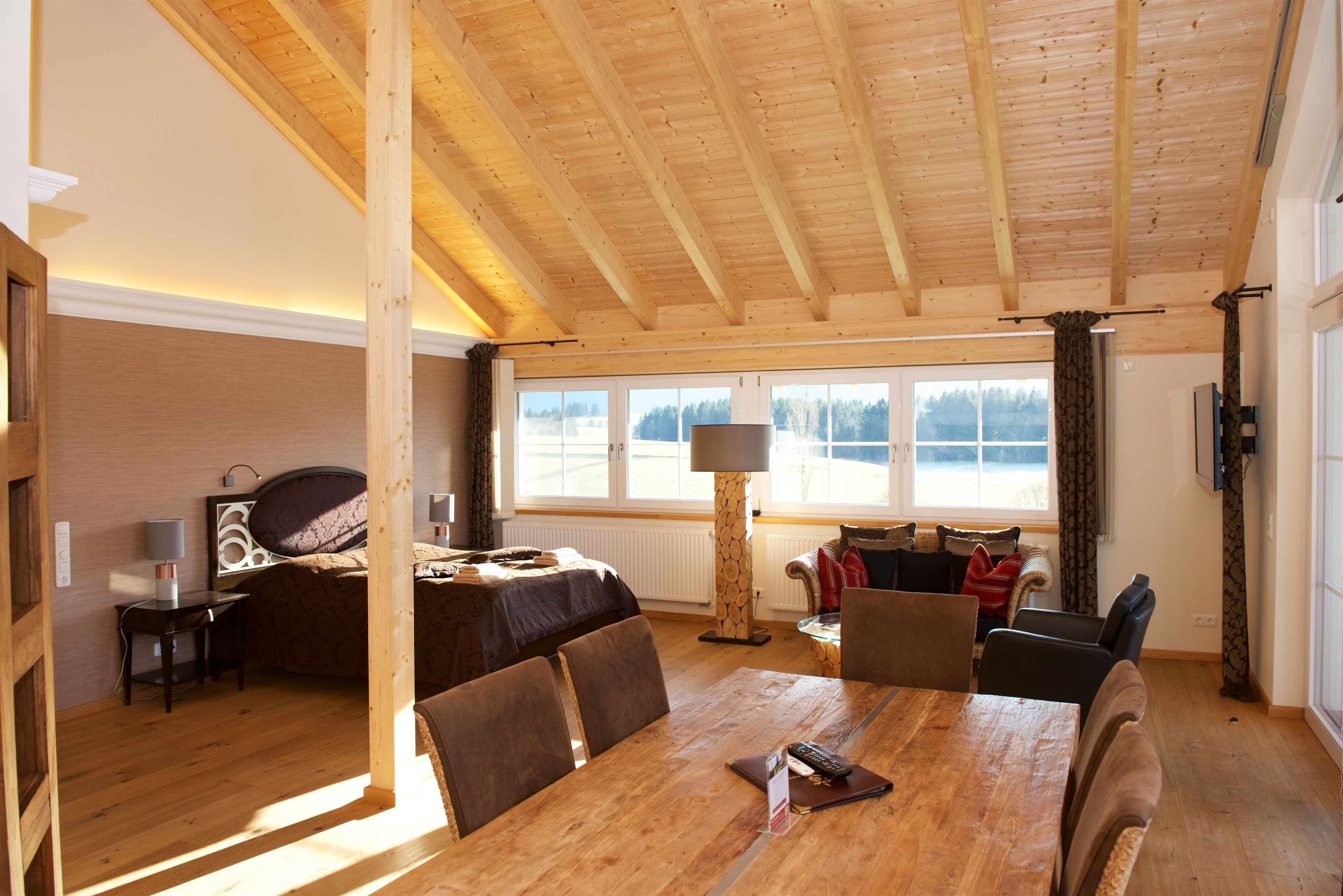 A spacious room with a wooden ceiling, a large dining table, and a cozy seating area with chairs.