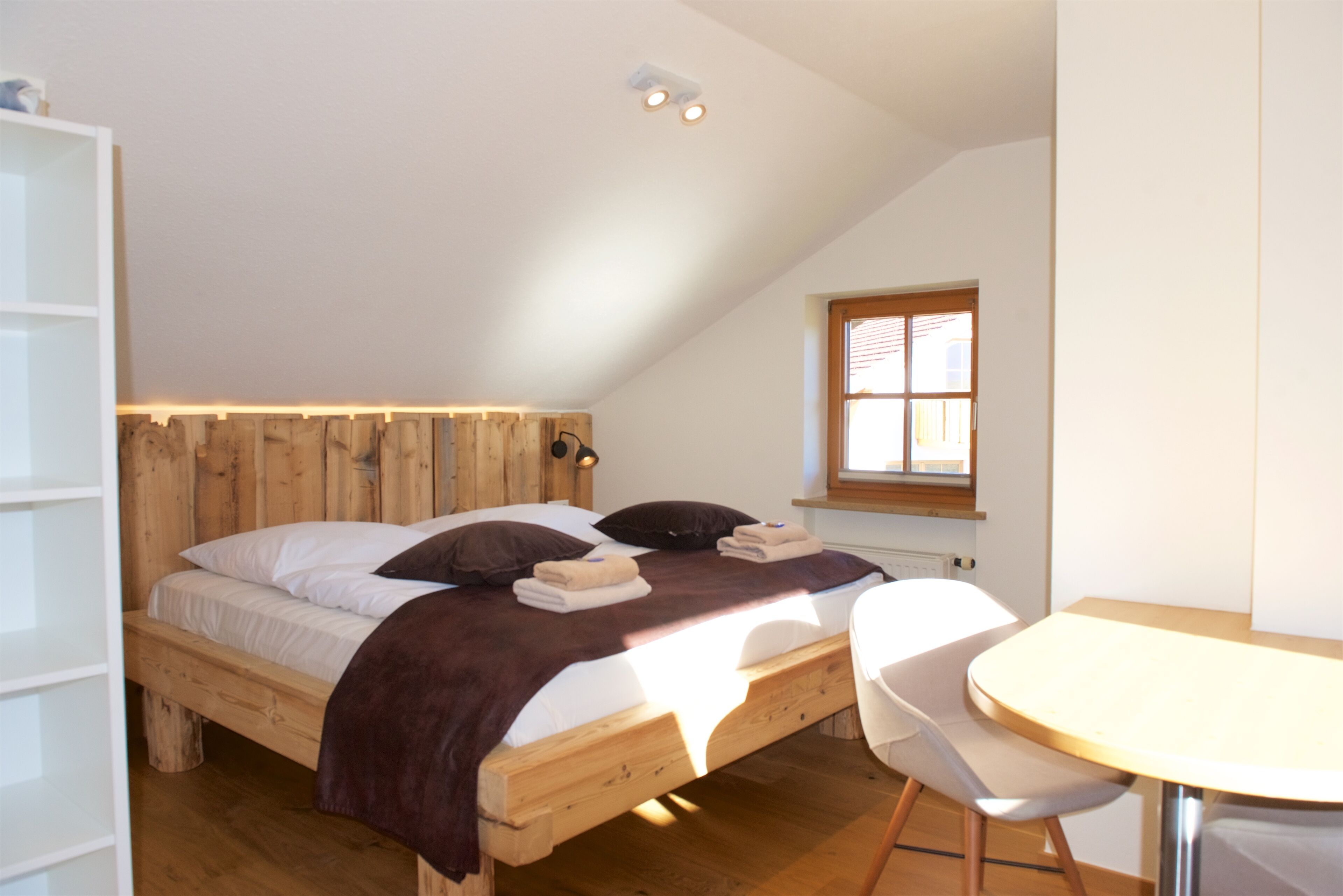 Ein Schlafzimmer mit einem Holzbett, einem kleinen Tisch und einem Fenster.