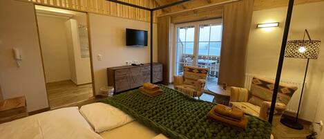 A hotel room with a bed, a TV, a desk, and a view of the sea.