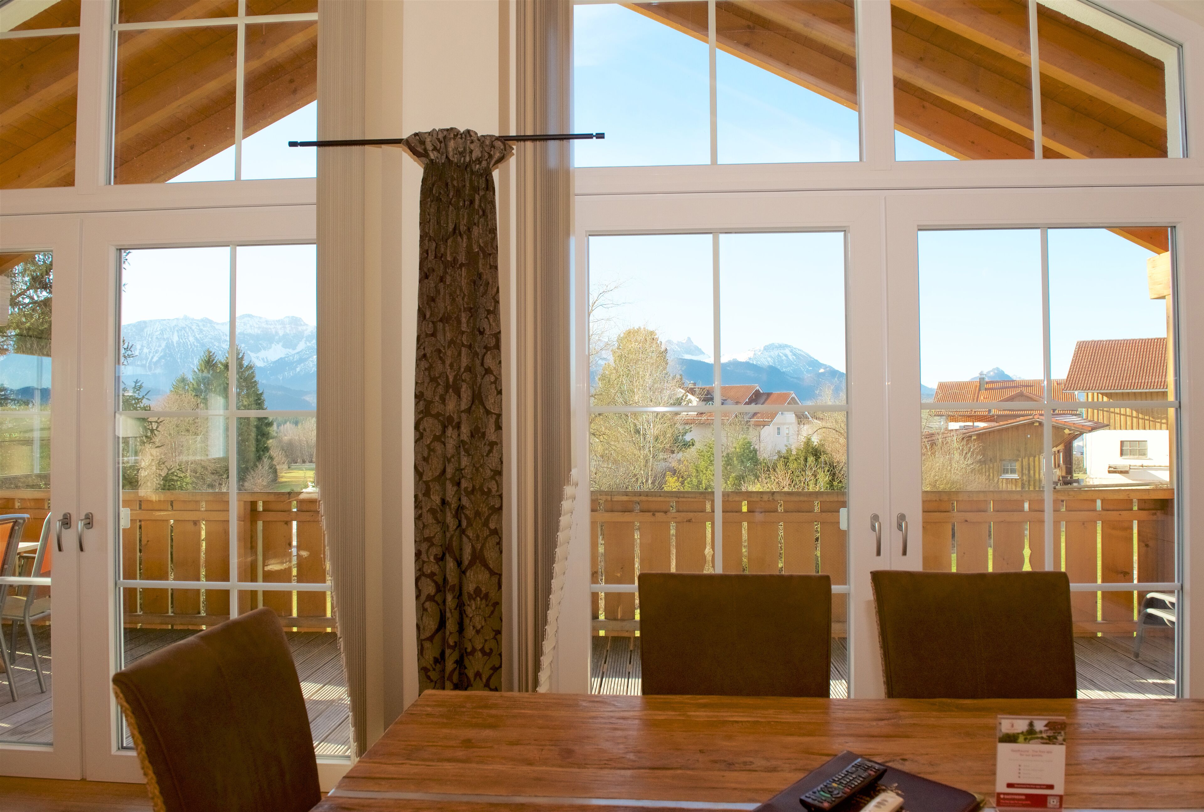 A dining area with a wooden table and chairs, large windows with a view of mountains and a wooden deck.