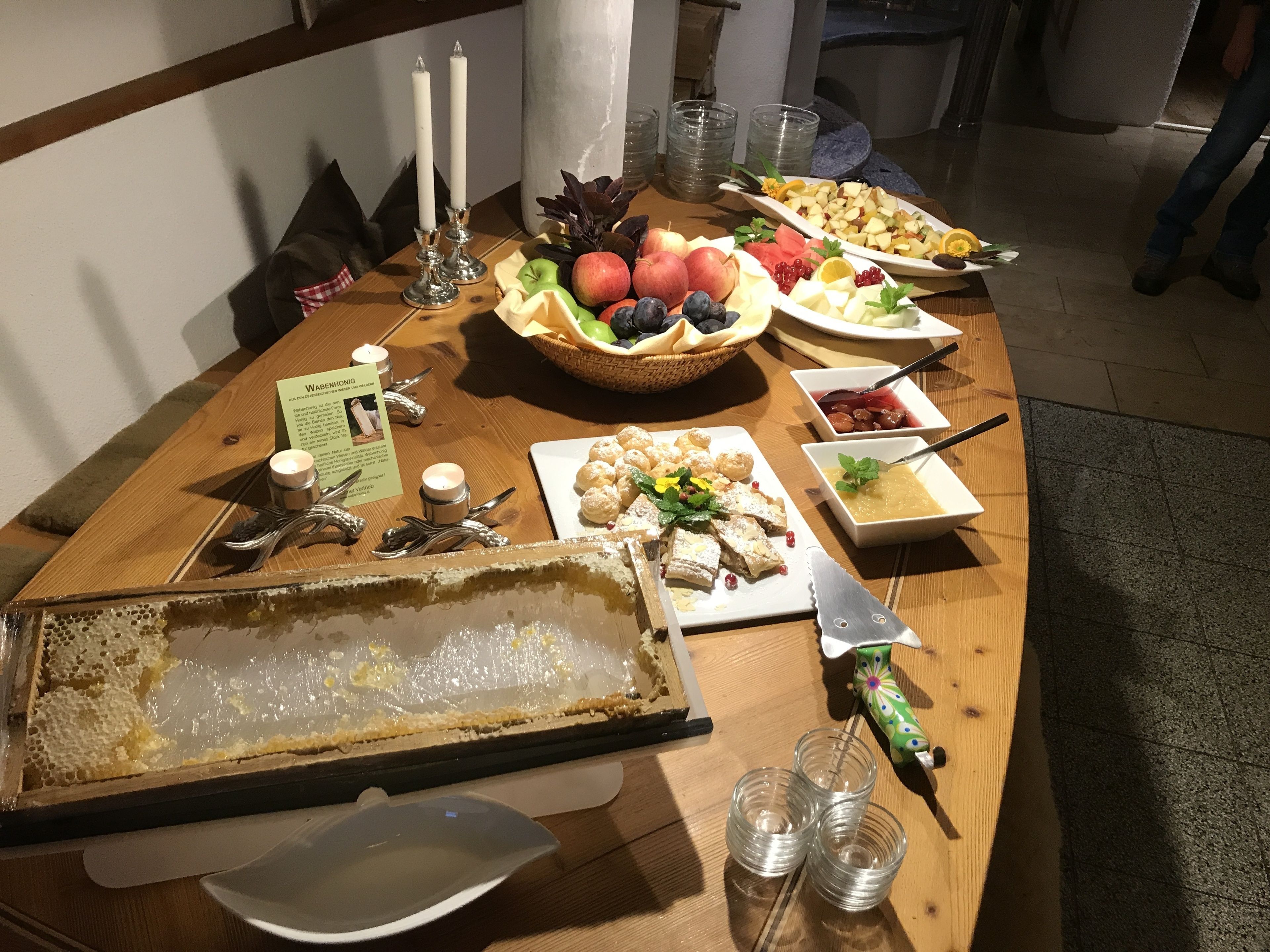 Una mesa de madera con diversos alimentos, como frutas, pasteles y una exhibición de panales.