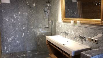 A modern bathroom with a marble shower wall, a wooden vanity, and a large mirror with a gold frame.
