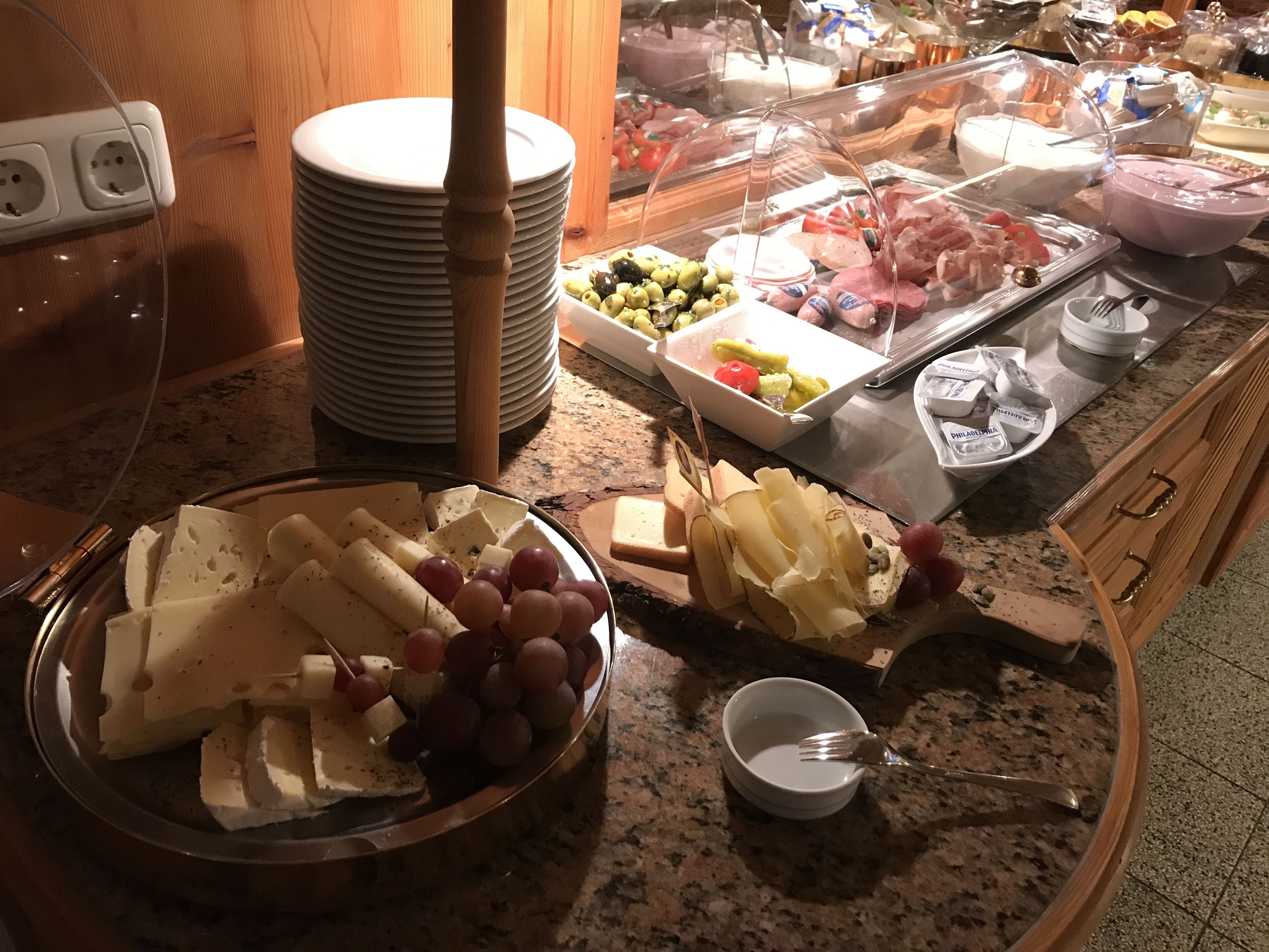 Una mesa de buffet con diversos alimentos, entre ellos queso, uvas y carnes.