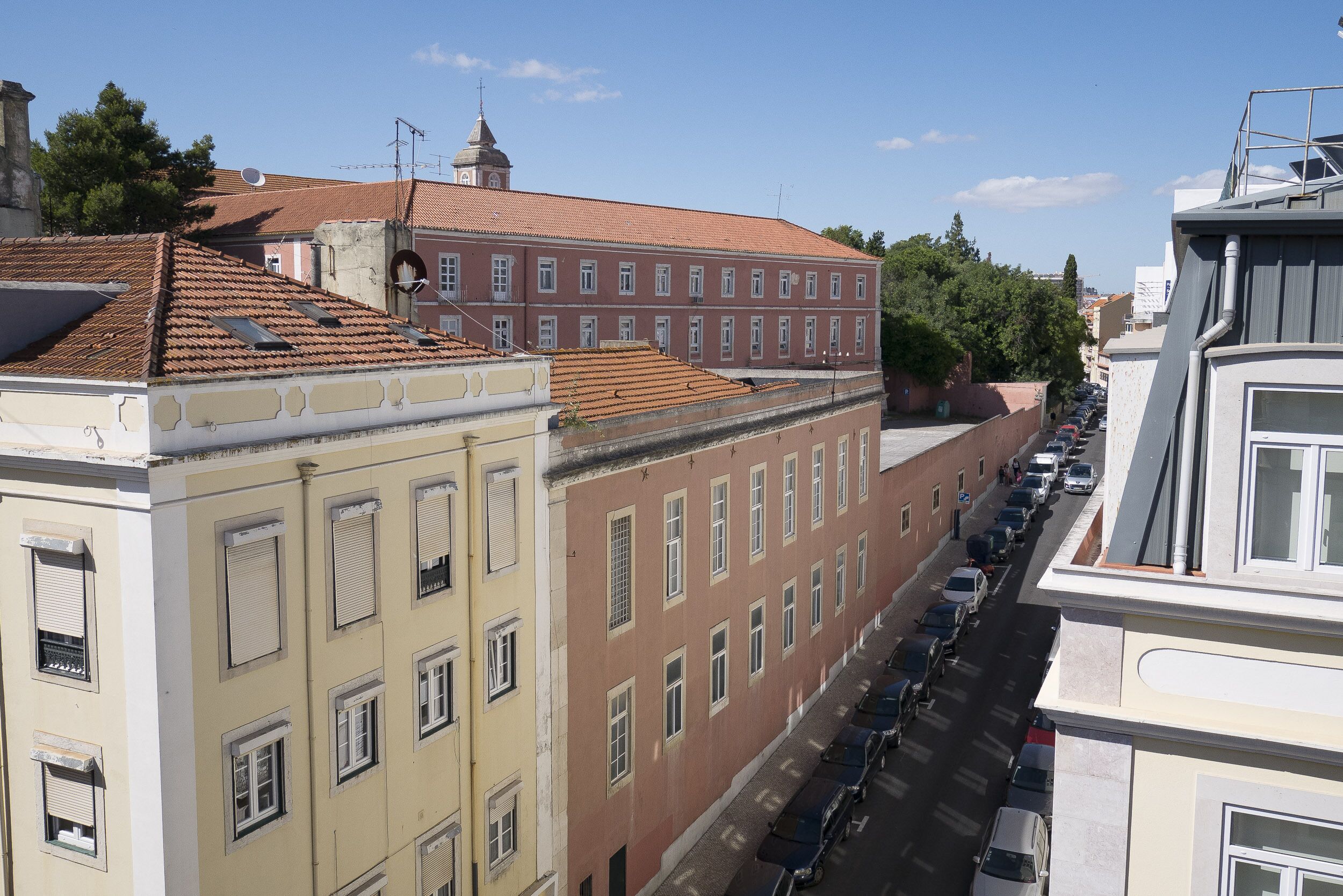 Una hilera de edificios con tejados rojos, una calle con coches aparcados y un cielo azul despejado.