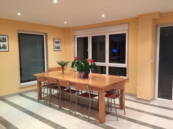 A dining area with a wooden table and chairs, a potted plant, and a window with a view.