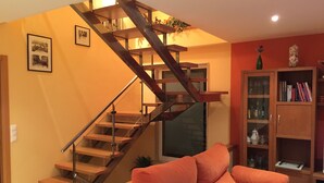 Una escalera con escalones de madera y barandillas de metal, un sofá, una estantería y cuadros en la pared.